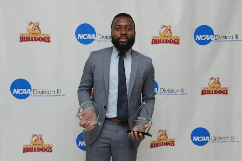 Jean-Luc holding two awards in front of an NCAA Division III Brooklyn Bulldogs backdrop